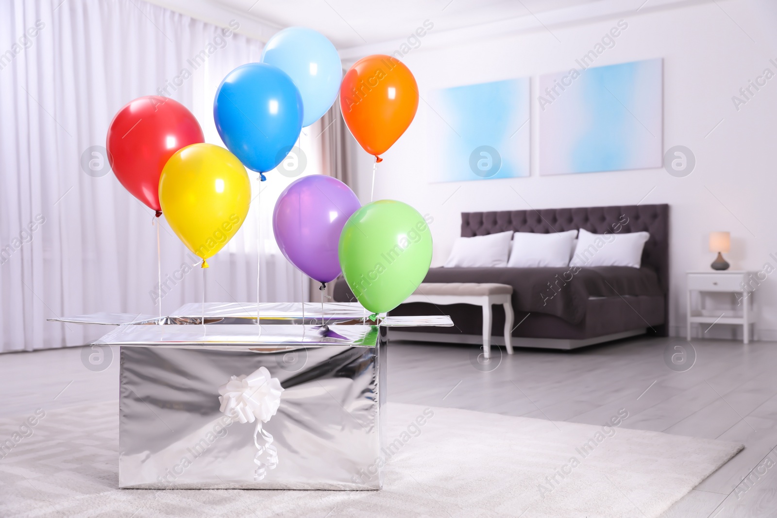 Photo of Gift box with bright air balloons in modern bedroom