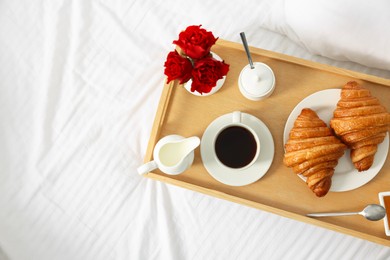 Photo of Tasty breakfast served in bed. Fresh croissants, coffee, honey and jam on wooden tray, space for text