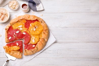 Photo of Tasty galette with citrus fruits served on white wooden table, flat lay. Space for text