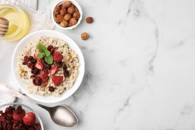 Photo of Oatmeal with freeze dried strawberries and mint served with honey and hazelnuts on white marble table, flat lay. Space for text