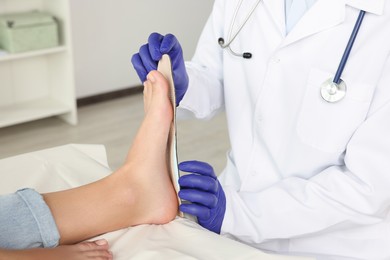 Photo of Male orthopedist fitting insole to patient's foot in hospital, closeup