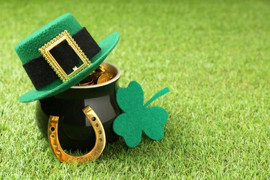 Photo of St. Patrick's day. Pot of gold with leprechaun hat, horseshoe and decorative clover leaf on green grass. Space for text