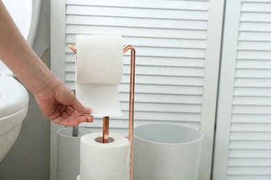 Photo of Woman taking toilet paper from roll holder in bathroom, closeup