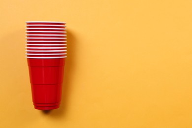 Photo of Red plastic cups on orange background, top view with space for text