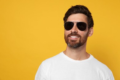 Photo of Portrait of smiling bearded man with stylish sunglasses on orange background. Space for text