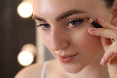 Photo of Makeup product. Woman applying black eyeliner indoors, closeup