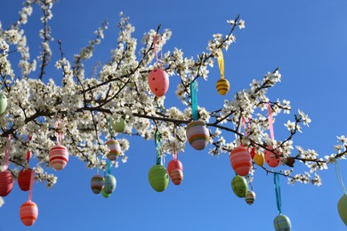 Photo of Beautifully painted Easter eggs hanging on blooming cherry tree against blue sky