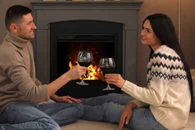 Photo of Lovely couple with glasses of wine spending time together on floor near fireplace at home