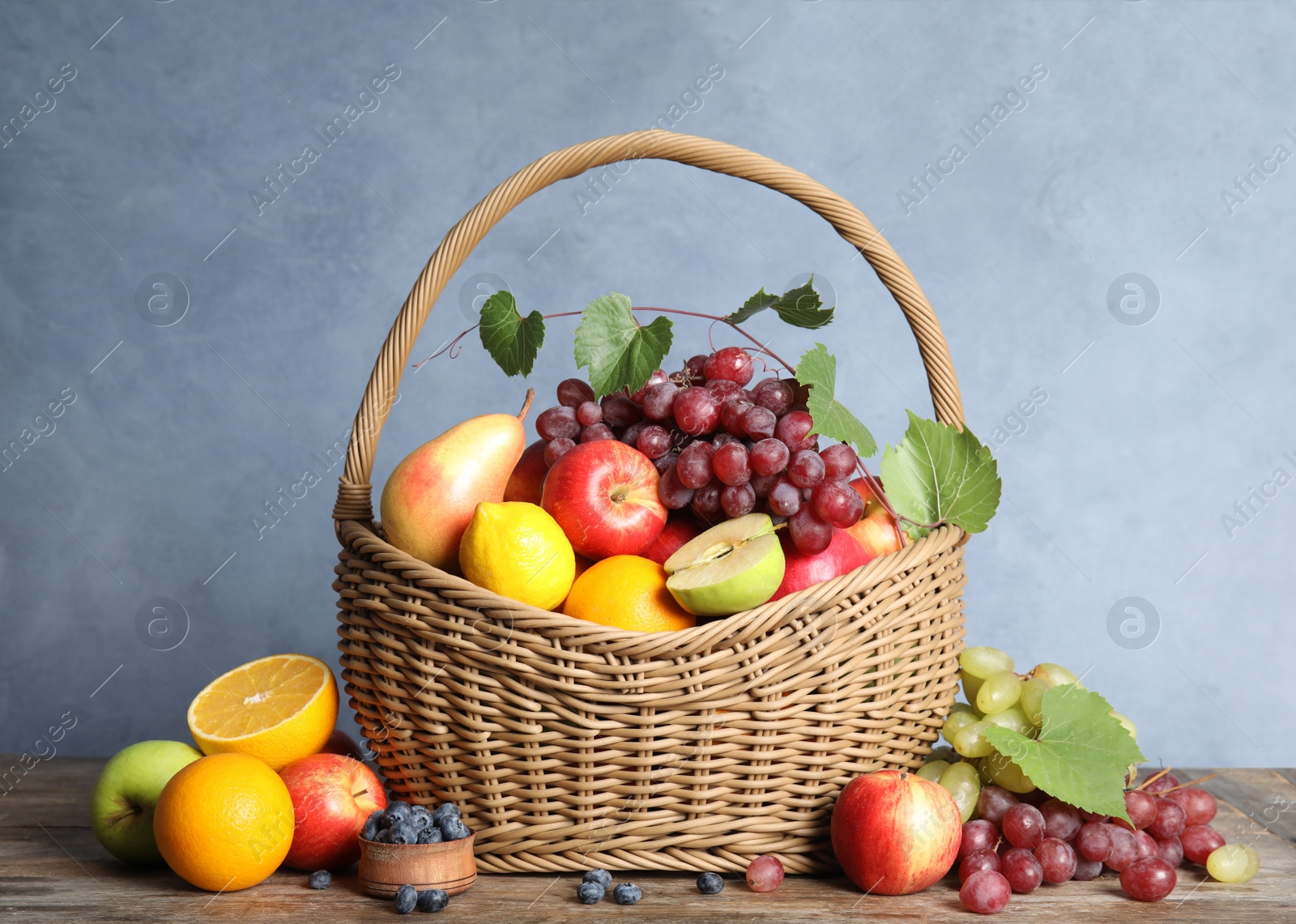 Photo of Wicker basket with different fruits and berries on wooden table near blue wall