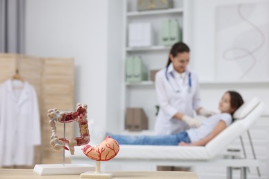 Photo of Gastroenterologist examining girl in clinic, focus on models of stomach and intestine on table