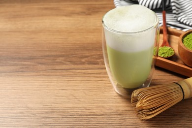 Photo of Glass of tasty matcha latte and bamboo whisk on wooden table, space for text
