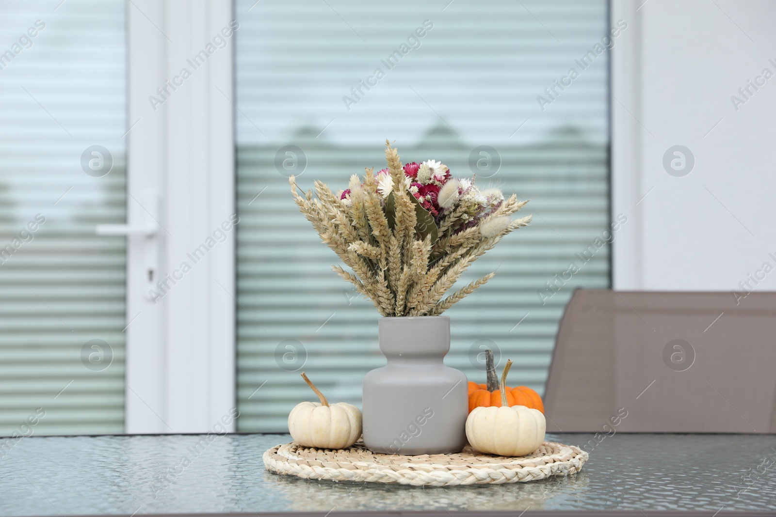 Photo of Beautiful bouquet of dry flowers and small pumpkins on glass table outdoors