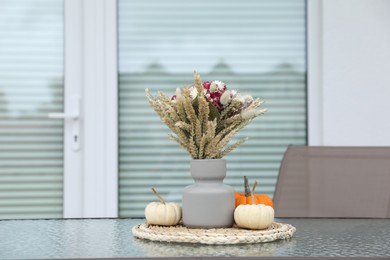 Photo of Beautiful bouquetdry flowers and small pumpkins on glass table outdoors