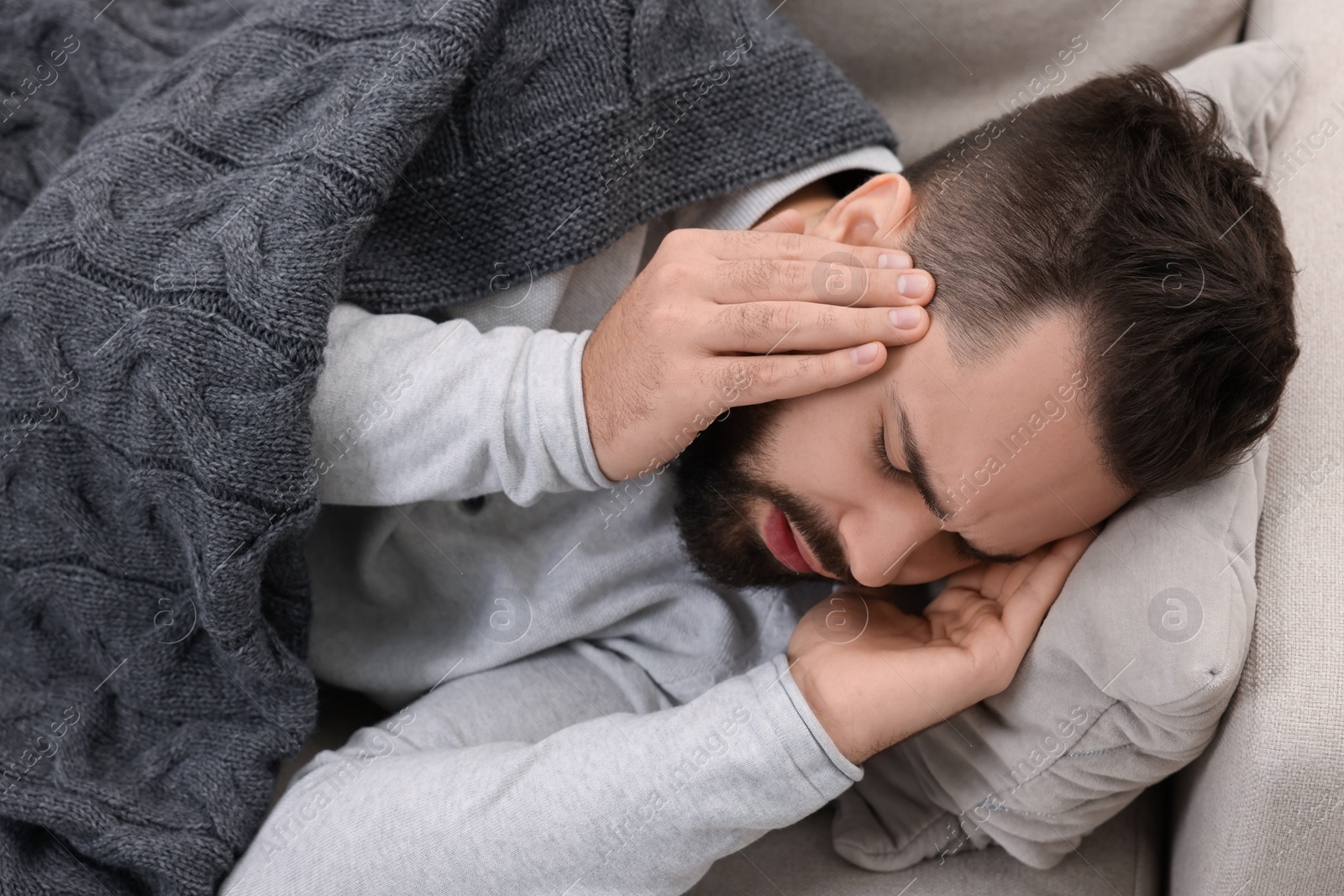 Photo of Man suffering from headache on sofa under blanket