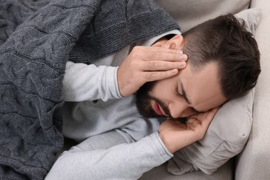 Man suffering from headache on sofa under blanket