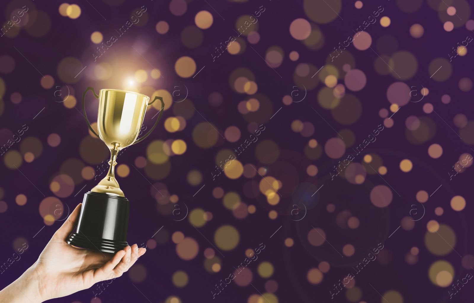 Image of Woman holding gold trophy cup on violet background, closeup. Space for text