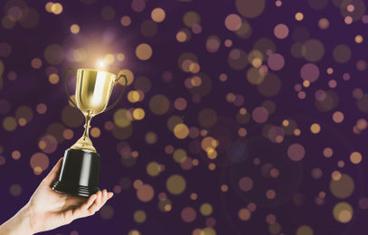 Image of Woman holding gold trophy cup on violet background, closeup. Space for text