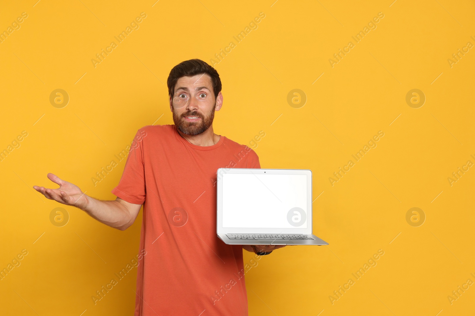 Photo of Handsome man with laptop on orange background