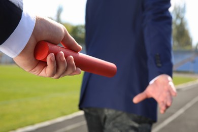 Photo of Businessman passing baton to his partner outdoors, closeup