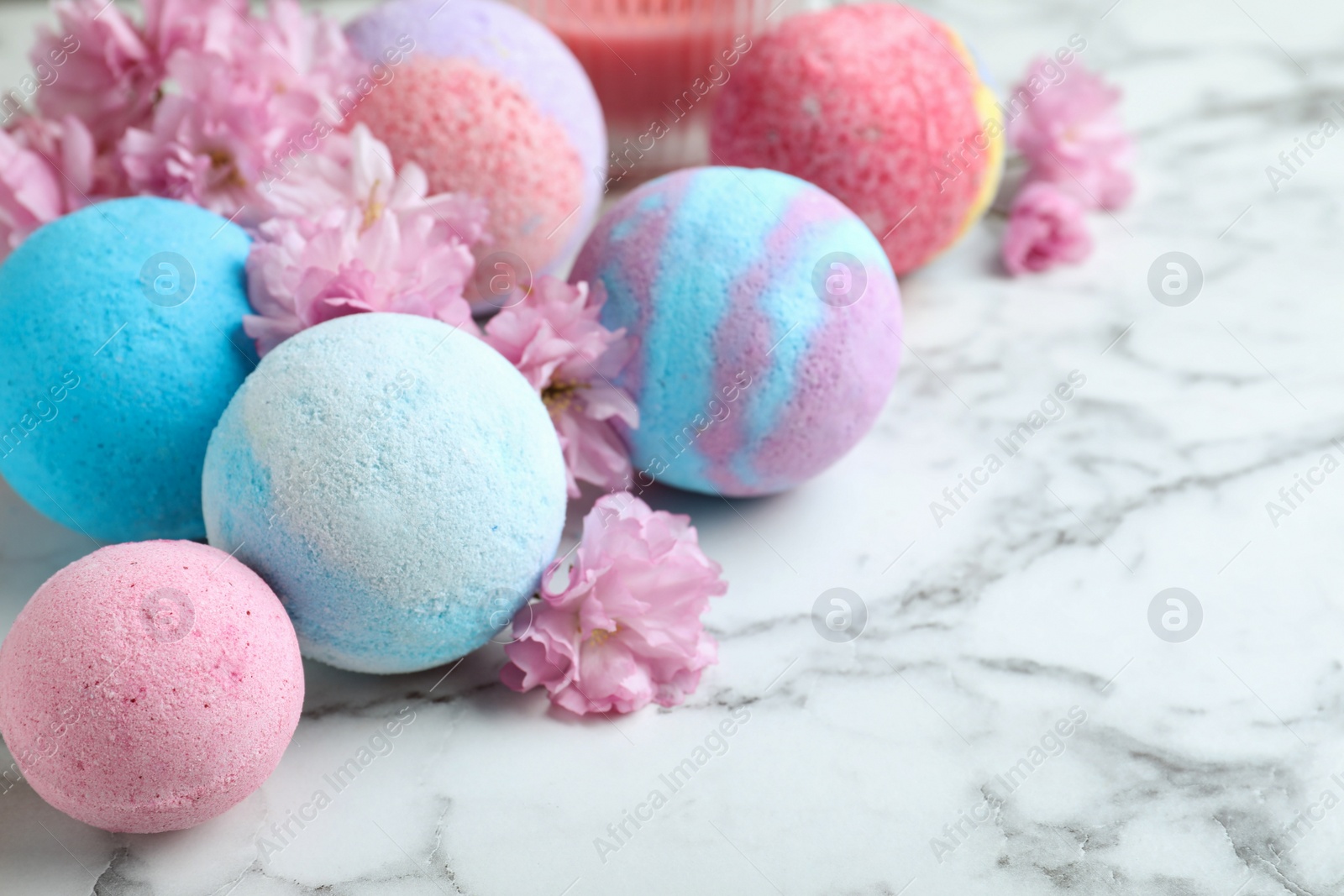 Photo of Fragrant bath bombs and sakura flowers on white marble table, closeup