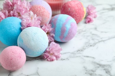 Photo of Fragrant bath bombs and sakura flowers on white marble table, closeup