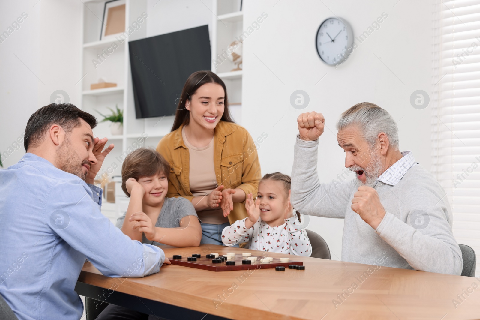 Photo of Emotional family playing checkers at wooden table in room