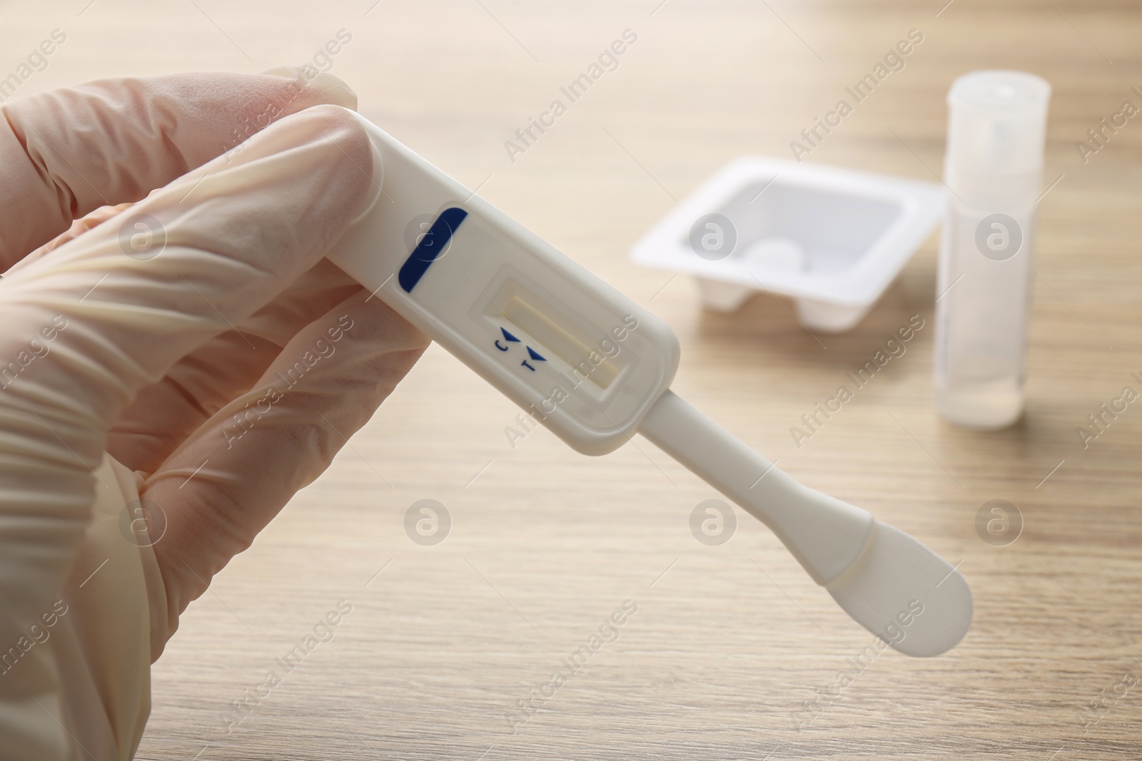 Photo of Woman holding disposable express test above wooden table, closeup