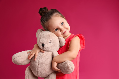 Cute little girl with teddy bear on pink background
