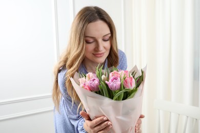 Happy young woman with bouquet of beautiful tulips indoors