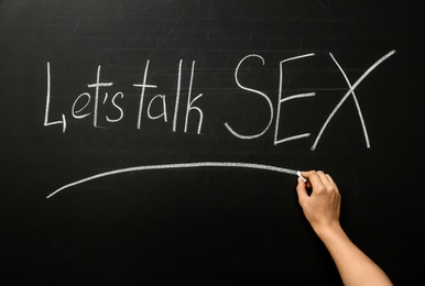 Photo of Woman writing phrase "LET'S TALK SEX" on blackboard. School education