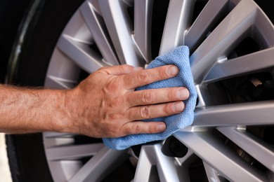 Photo of Man cleaning car wheel with rag, closeup