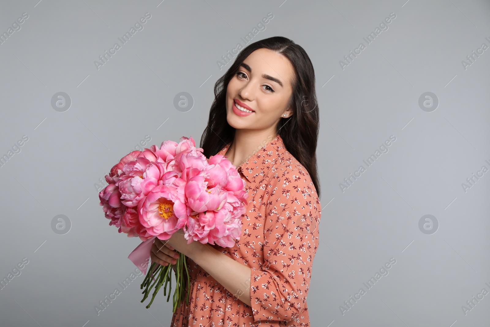 Photo of Beautiful young woman with bouquet of peonies on light grey background