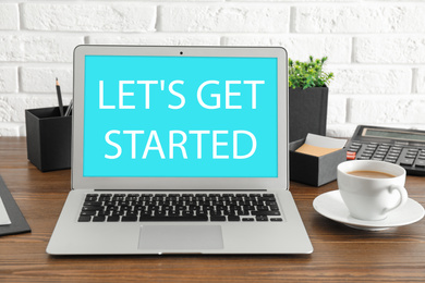 Modern laptop with phrase LET'S GET STARTED and cup of coffee on table