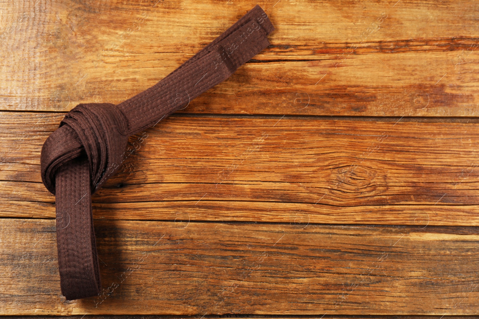 Photo of Brown karate belt on wooden background, top view. Space for text