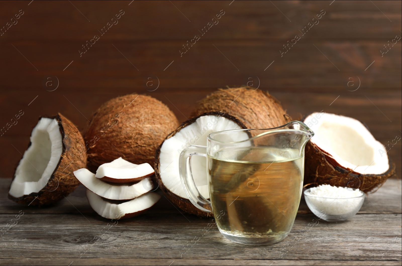 Photo of Jug of natural organic oil and coconuts on brown wooden table