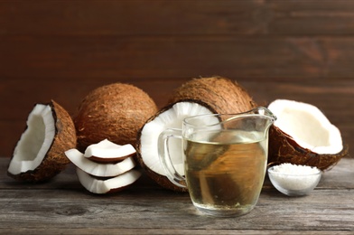 Photo of Jug of natural organic oil and coconuts on brown wooden table