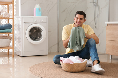 Man with clean clothes near washing machine in bathroom. Laundry day