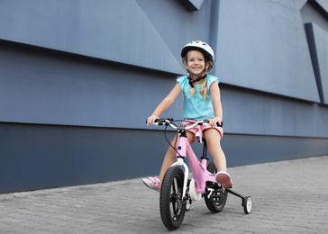 Little girl riding bicycle on street near gray wall