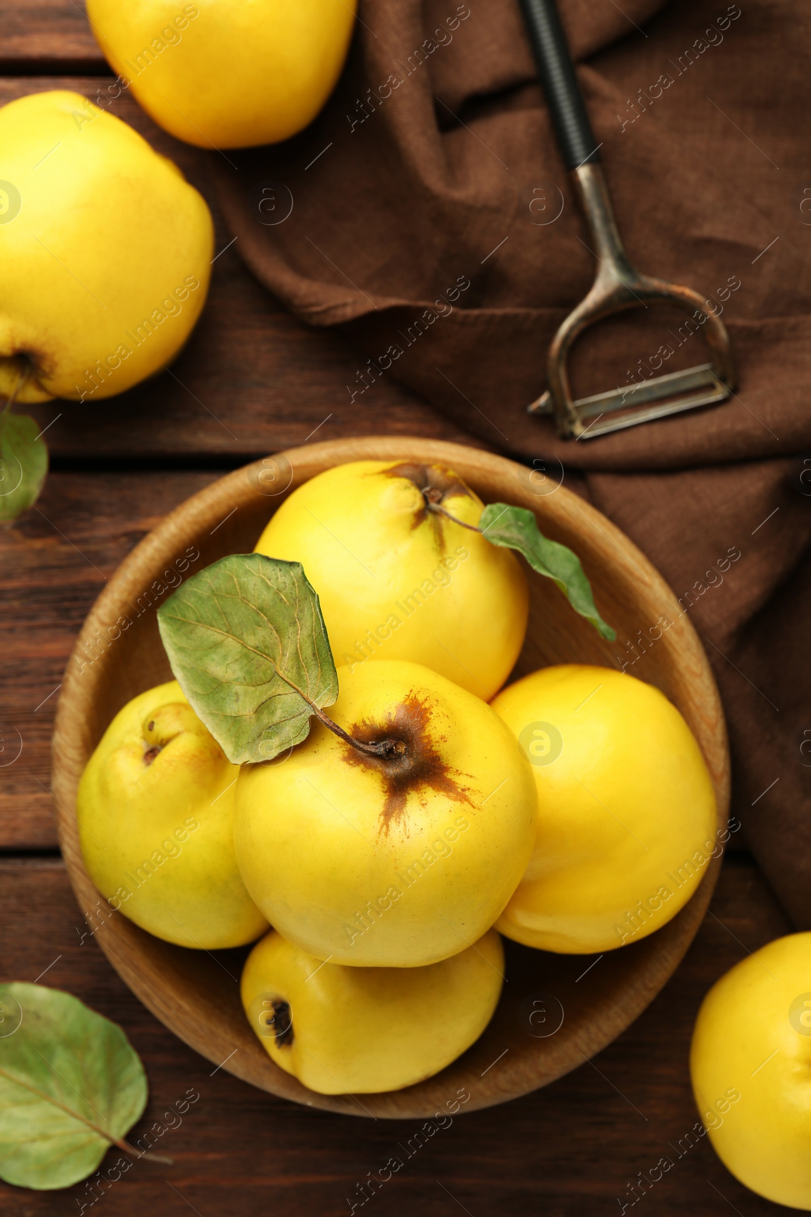 Photo of Tasty ripe quince fruits in bowl and peeler on wooden table, flat lay