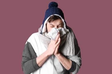 Man in warm clothes suffering from cold on color background