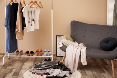 Photo of Messy dressing room with wardrobe rack and stylish armchair