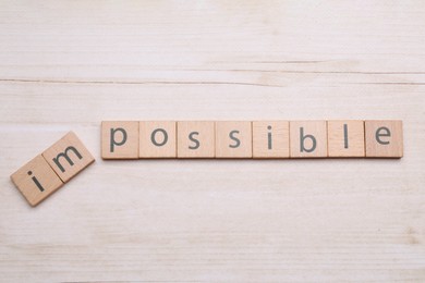 Photo of Motivation concept. Changing word from Impossible into Possible by removing squares on light wooden table, flat lay