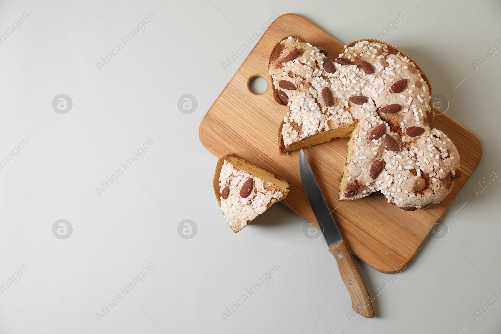 Photo of Board with cut delicious Italian Easter dove cake (traditional Colomba di Pasqua) on light grey table, top view. Space for text