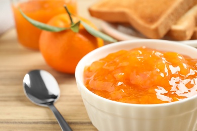Tasty tangerine jam in bowl on wooden table, closeup
