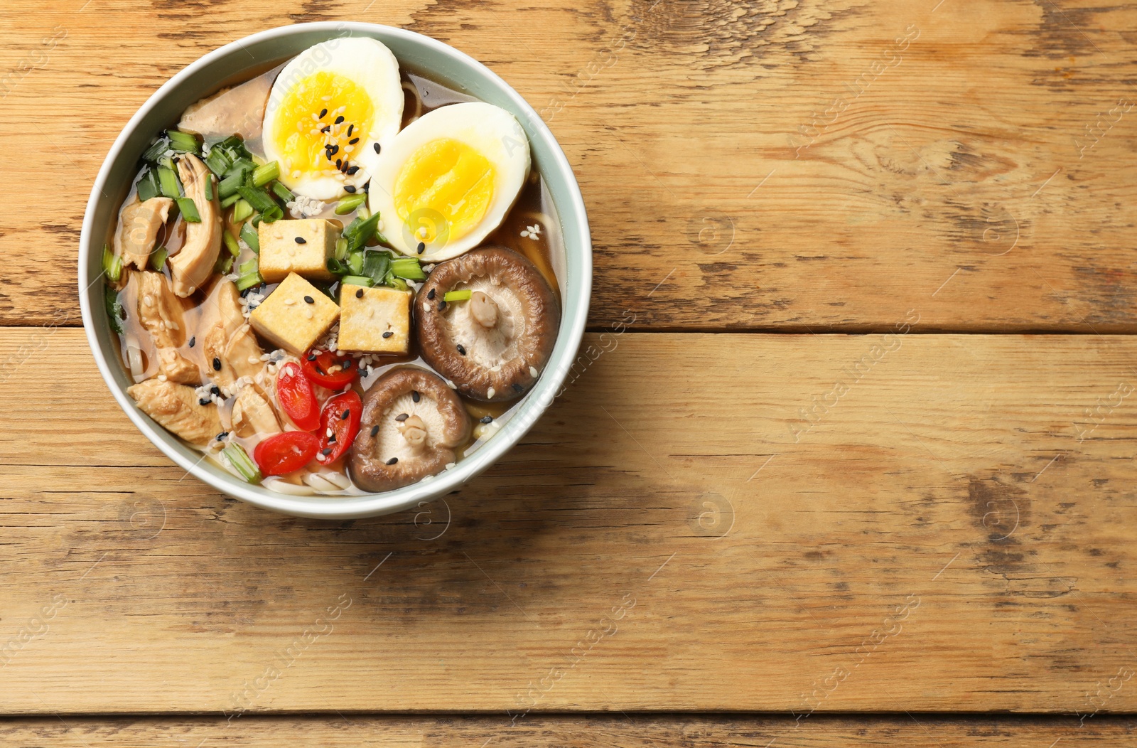 Photo of Bowl of delicious ramen on wooden table, top view with space for text. Noodle soup