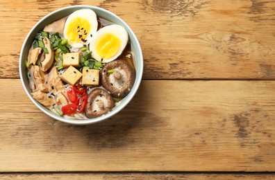 Bowl of delicious ramen on wooden table, top view with space for text. Noodle soup