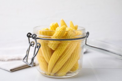 Photo of Tasty fresh yellow baby corns in glass jar on white tiled table, closeup