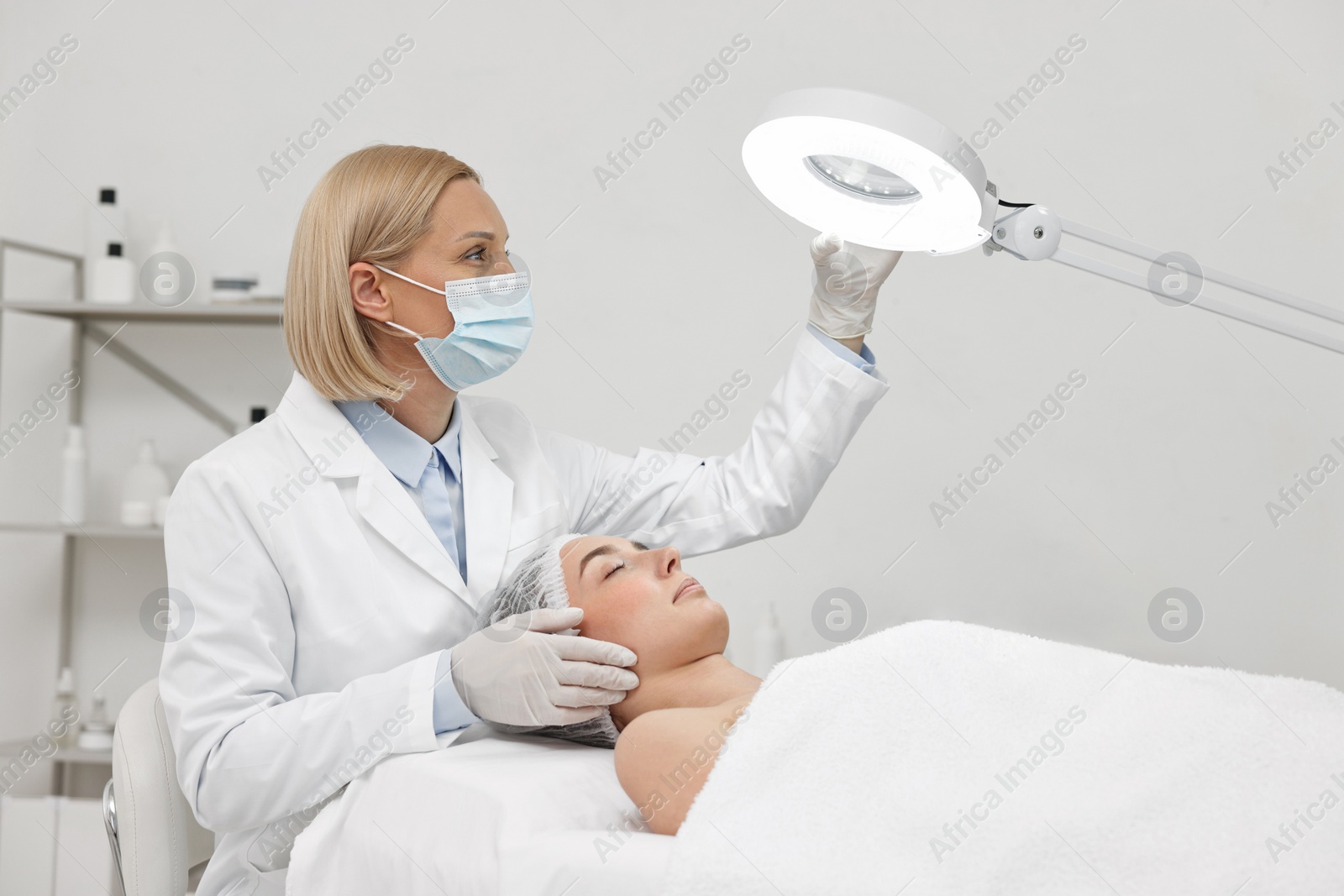 Photo of Dermatologist examining patient`s face under lamp in clinic