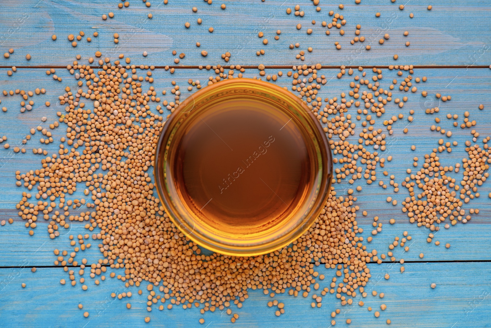Natural oil and mustard seeds on light blue wooden table, flat lay Photo of Natural oil and mustard seeds on light blue wooden table, flat lay