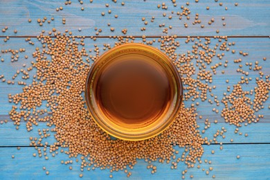 Photo of Natural oil and mustard seeds on light blue wooden table, flat lay
